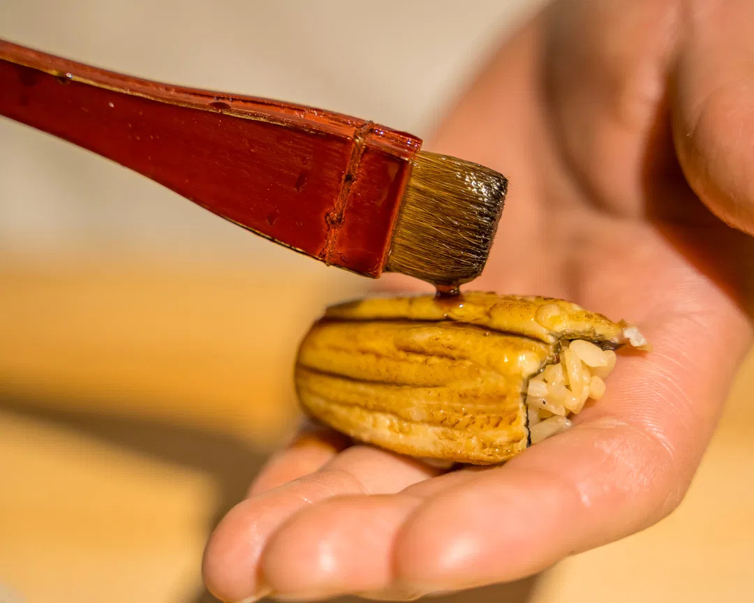 A piece of sushi being delicately brushed with soy sauce.