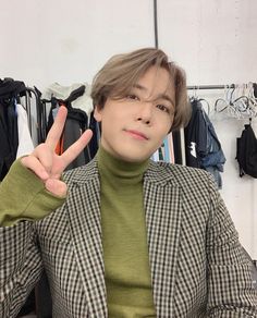 This contains a picture of Hongki in a green turtle neck sweater is making the peace sign with his hand