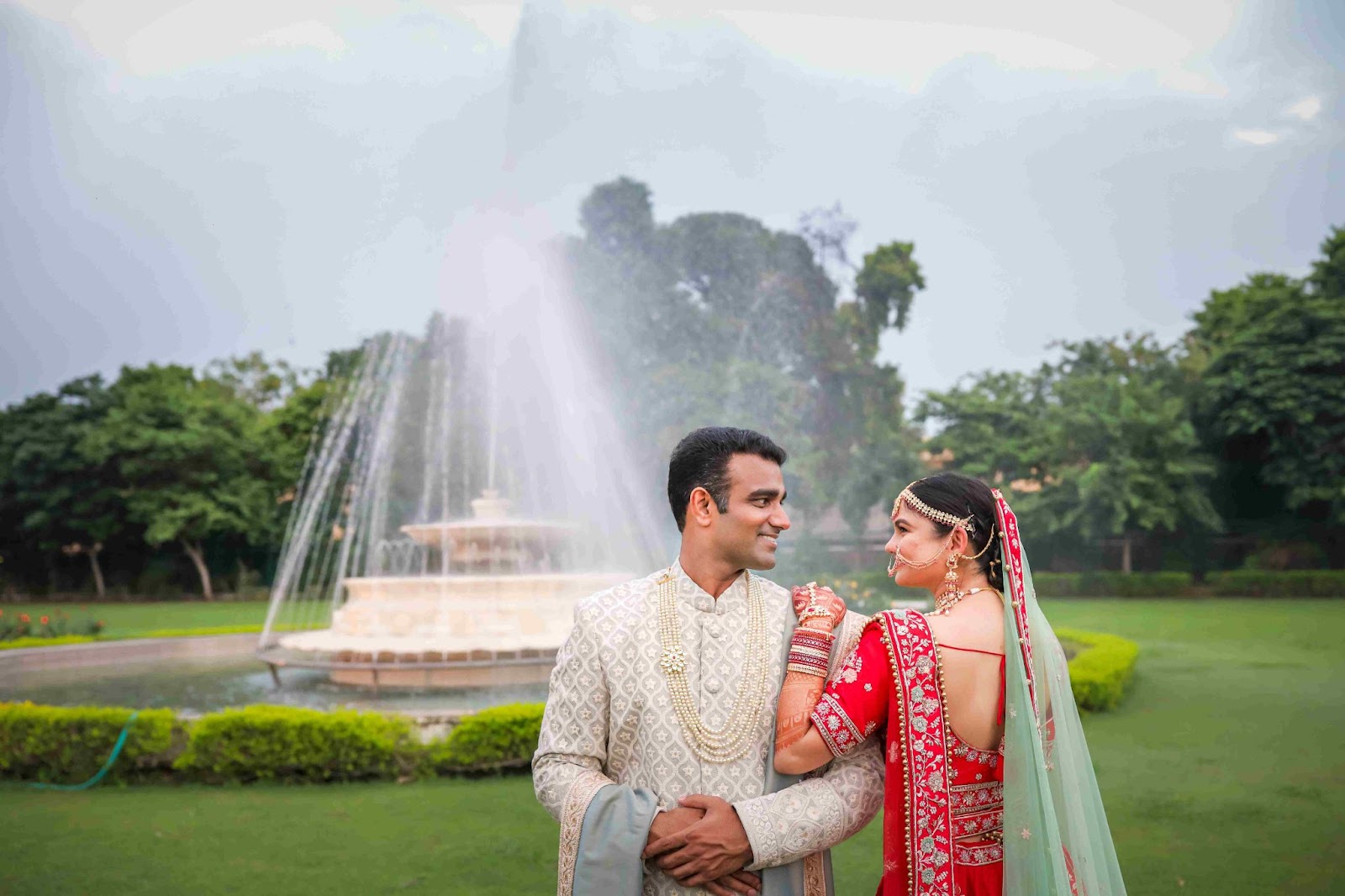 Wedding couple standing in a serene garden with a fountain, capturing timeless memories.