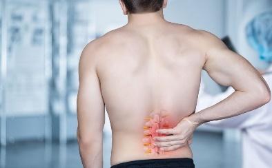 Hombre, con una de las enfermedades de la columna vertebral, apretándose la parte lumbar por la molestia que siente.