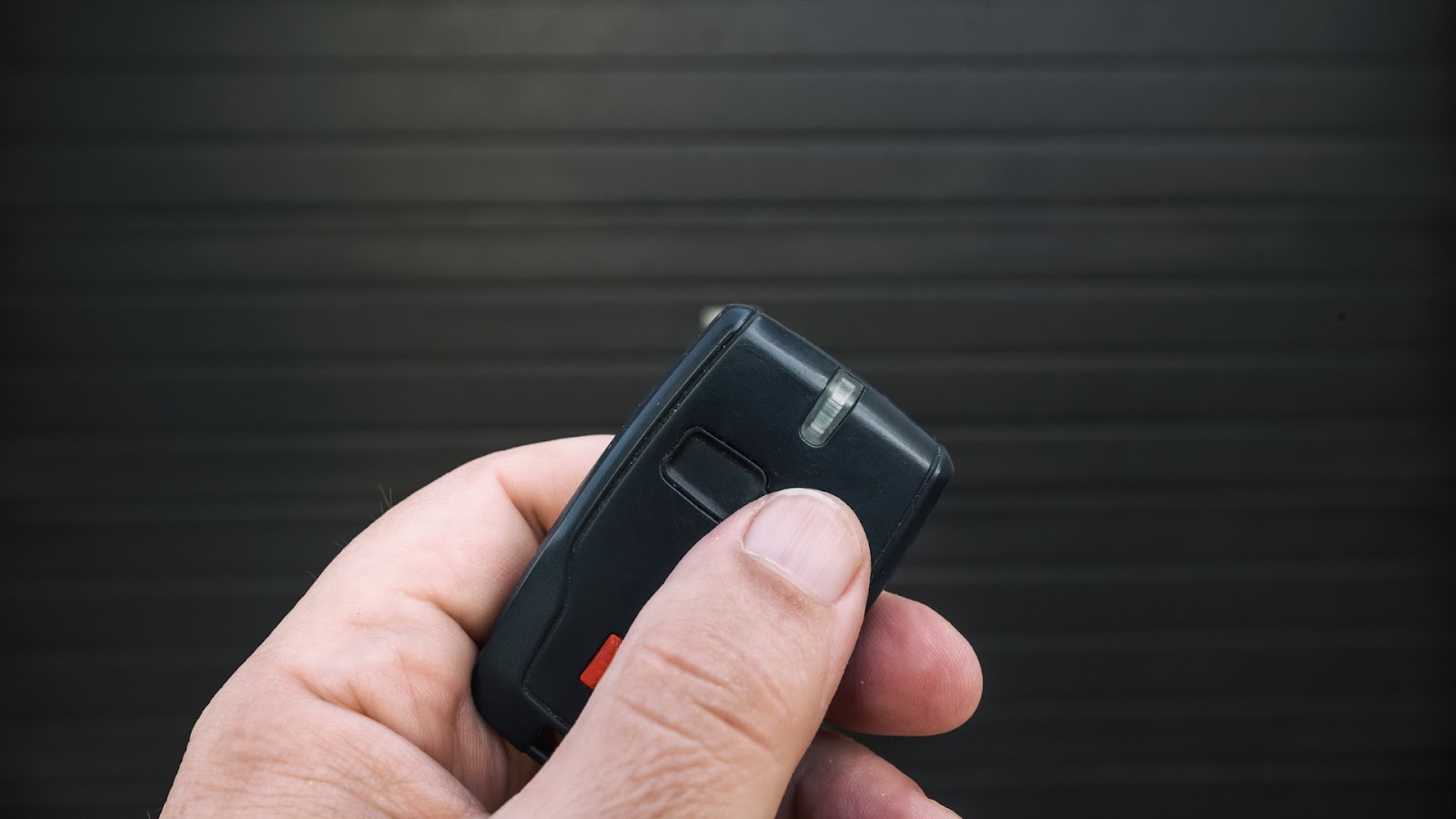 Hand pressing garage remote control with garage door not opening in background.
