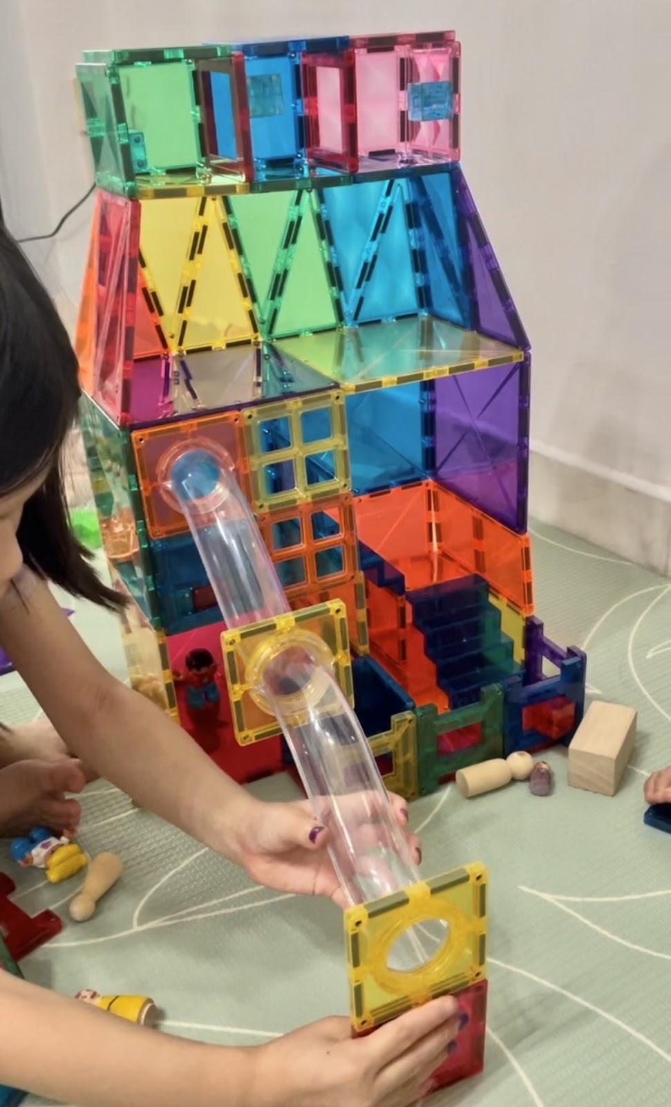 A child is deeply focused on constructing a colorful magnetic tile structure that features a ball run component, showcasing their concentration and engineering skills.
