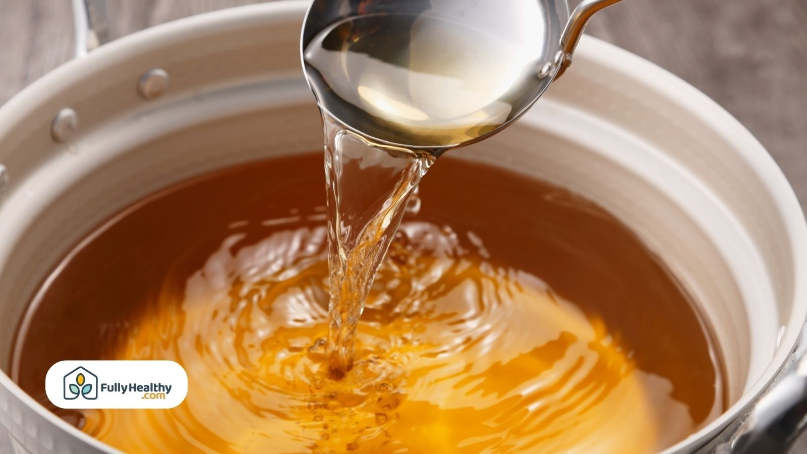 Clear hot broth being poured with a metal ladle into a pot