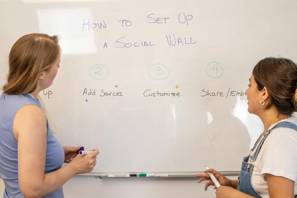 two women standing in front of a white board