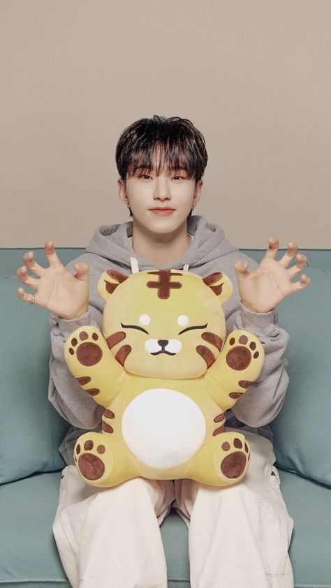 This contain SEVENTEEN's Hoshi sitting on top of a blue couch holding a stuffed animal in front of his face