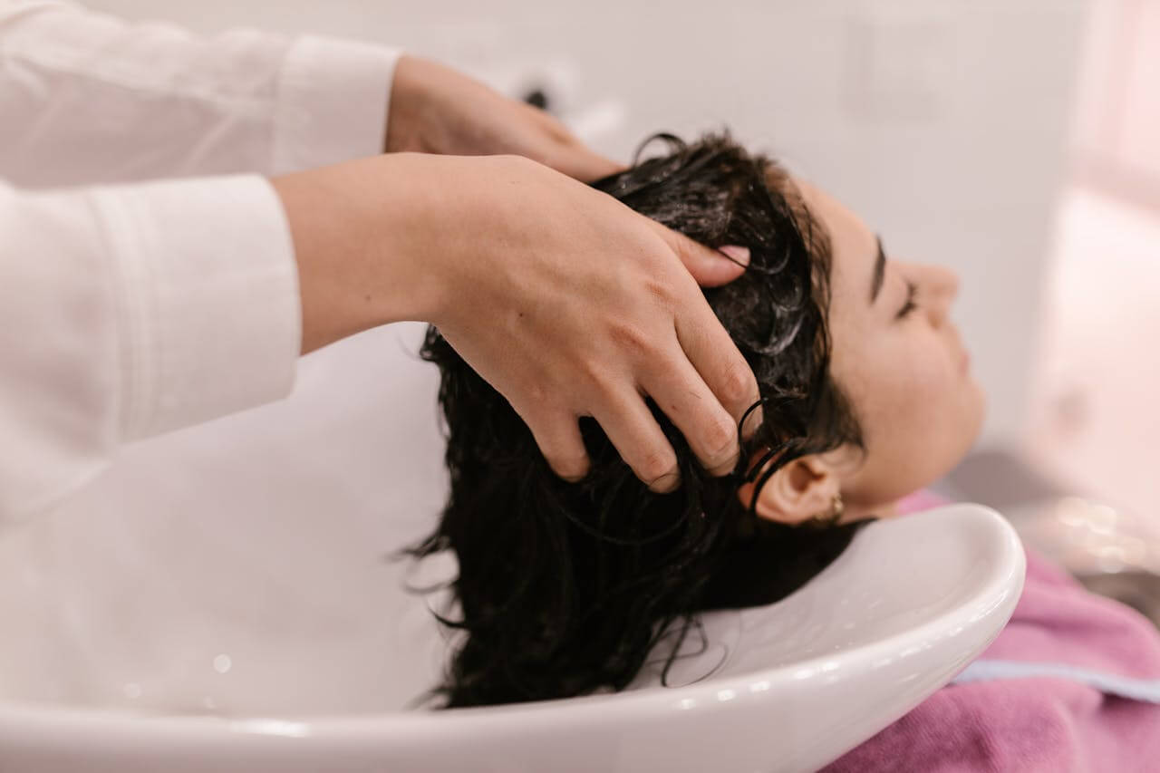 A woman enjoys a relaxing hair wash in a sink, benefiting from a soothing scalp massage with herbal oils.