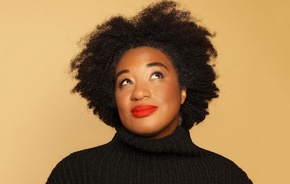 Headshot of Aja Barber wearing a black turtleneck with a beige backdrop. 