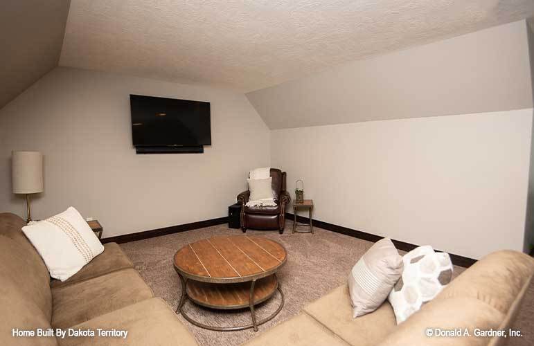 The bonus room is furnished with a V-shaped sectional, a round coffee table, and a leather armchair.