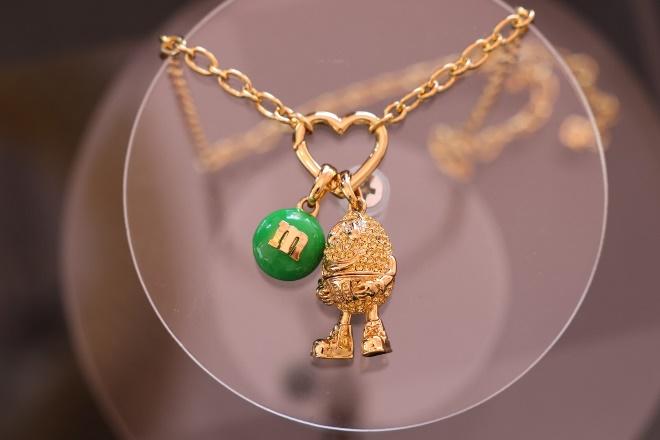 A gold necklace with a green m and a green ball

Description automatically generated