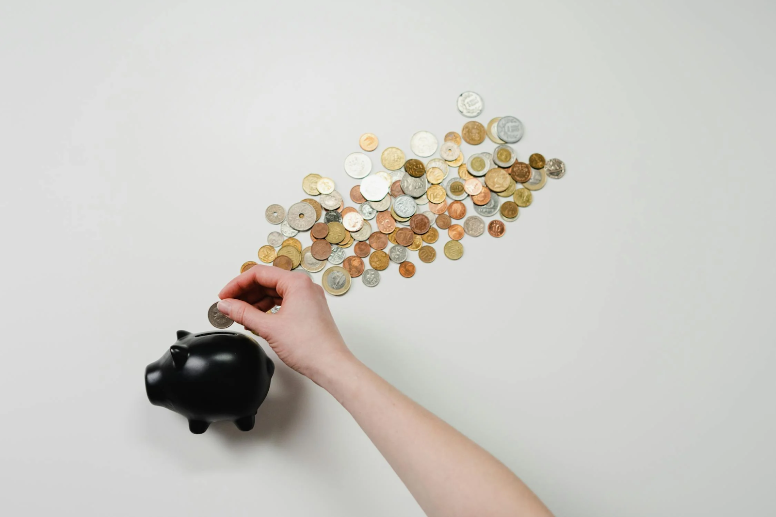 A person putting coins in a black piggy bank 