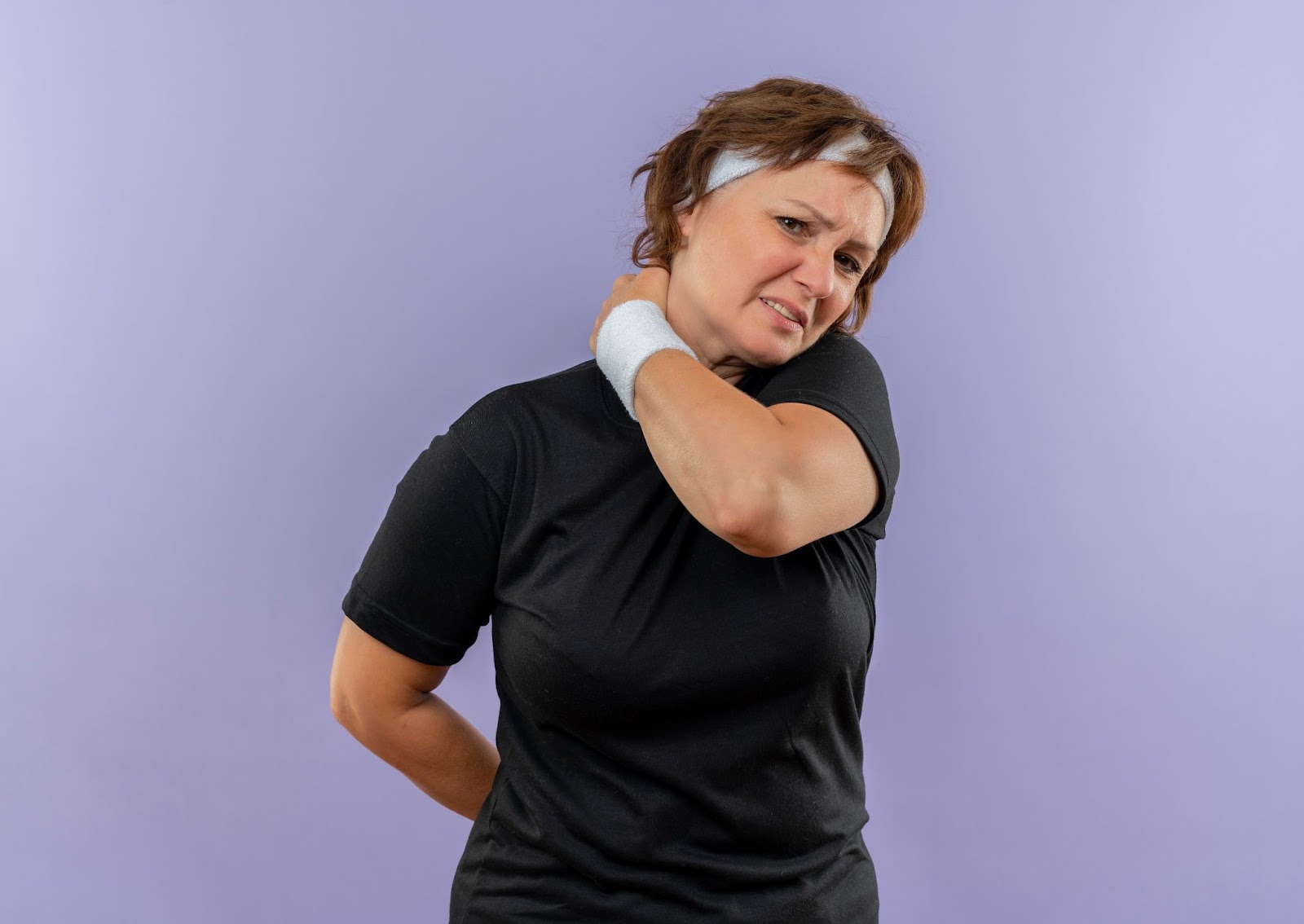A woman in workout clothes holds her neck because of muscle spasms.