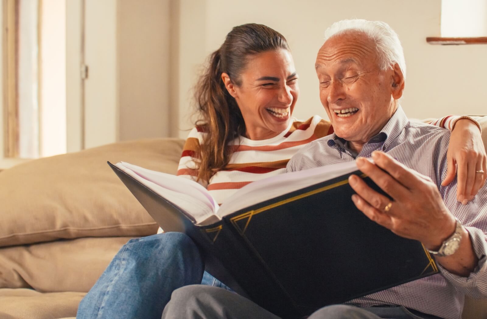 A woman and a senior with dementia looking through a photo album together, smiling and laughing.