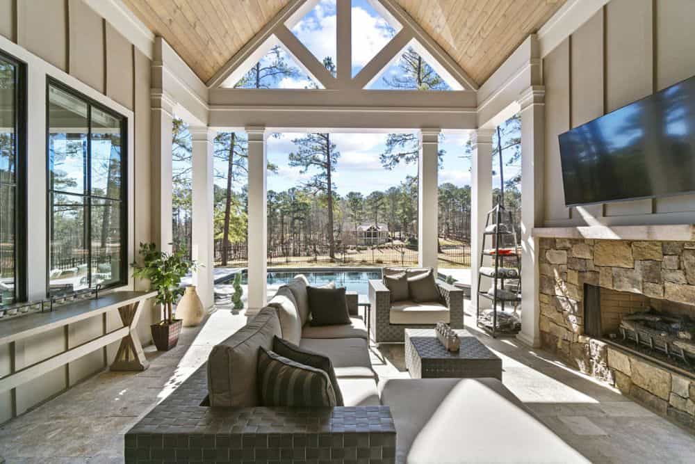 Rear covered porch with wicker seats, a stone fireplace, and a wall-mounted TV.