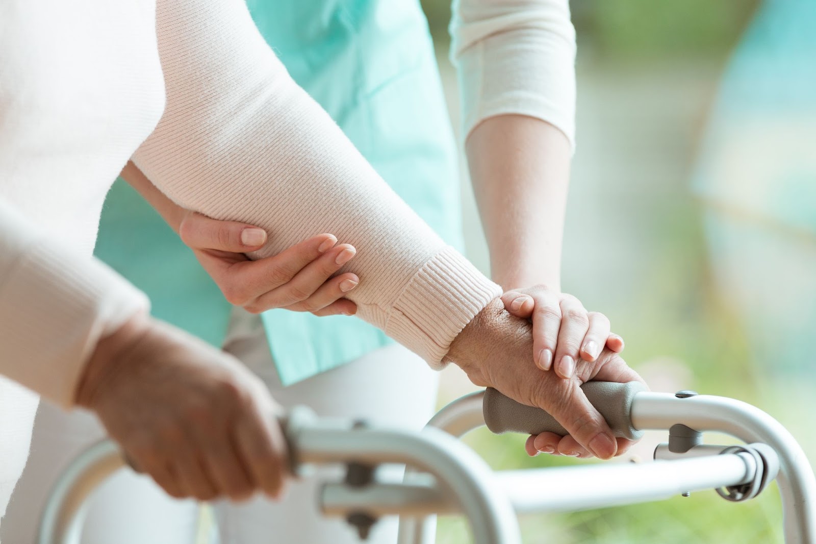 Closeup of a senior's hands holding a walker and supporting nurse helping them.