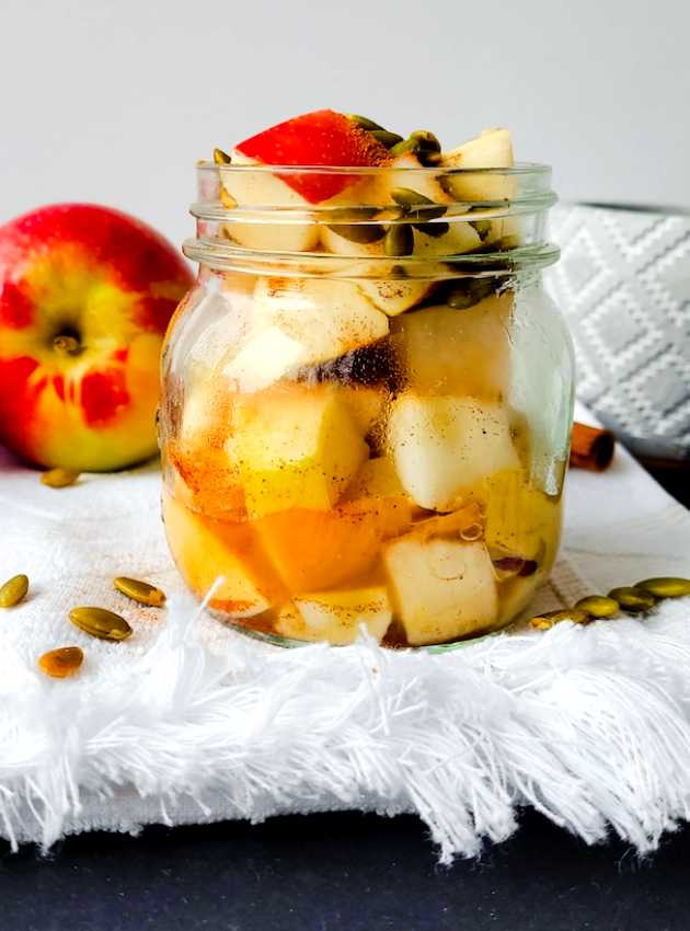 Mason jar filled with diced apples, seeds, and cinnamon, with a fresh apple in the background.