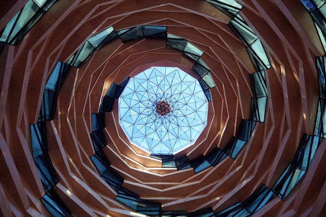 A view from below reveals a spiraling architectural marvel leading to a geometric, domed skylight with a honeycomb pattern. This example of computational design showcases concentric rings of windows and brown panels, creating a dynamic, swirling effect that sets the stage for the future of design.