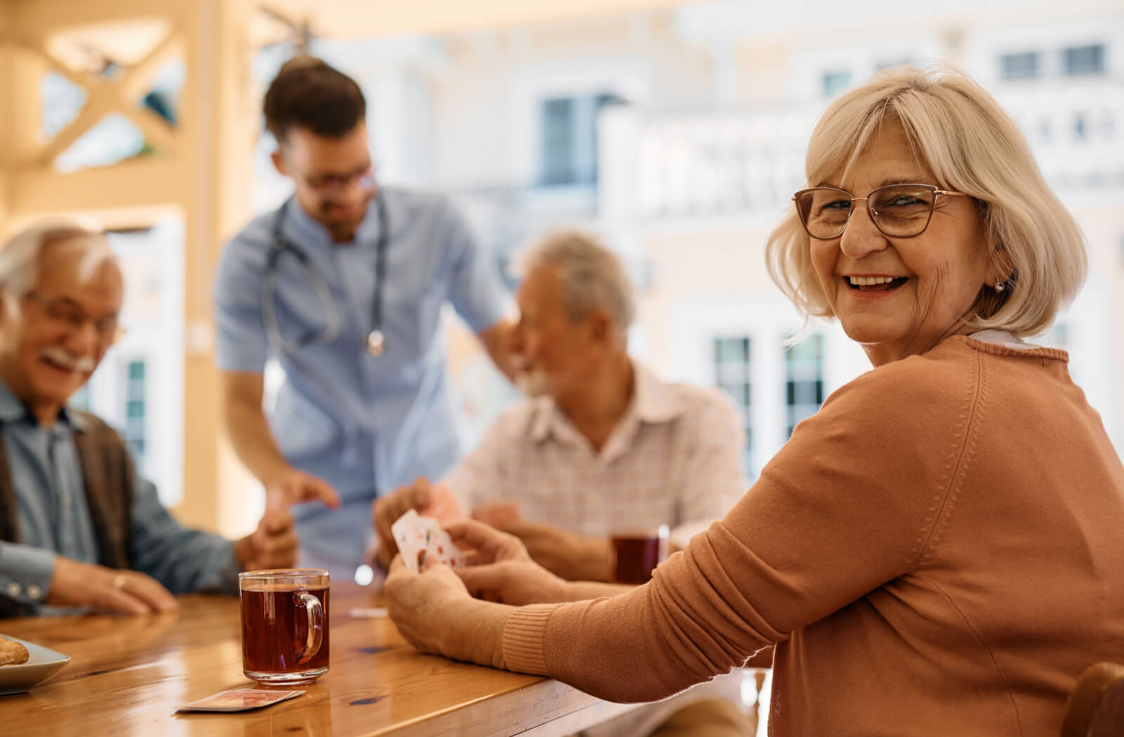 A group of seniors laughing while playing cards and drinking coffee on a patio in respite care.