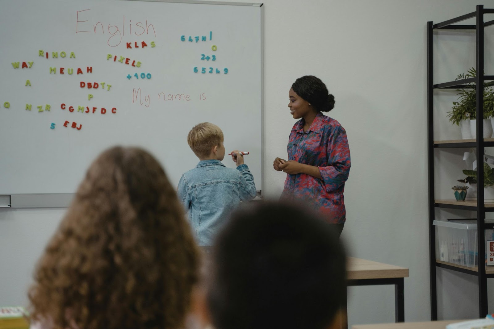 A female teacher helping a young student write on the board