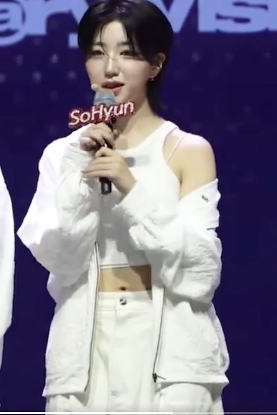 This contains an image of  tripleS Sohyun on a white cloth and she is holding a mic close to her mouth