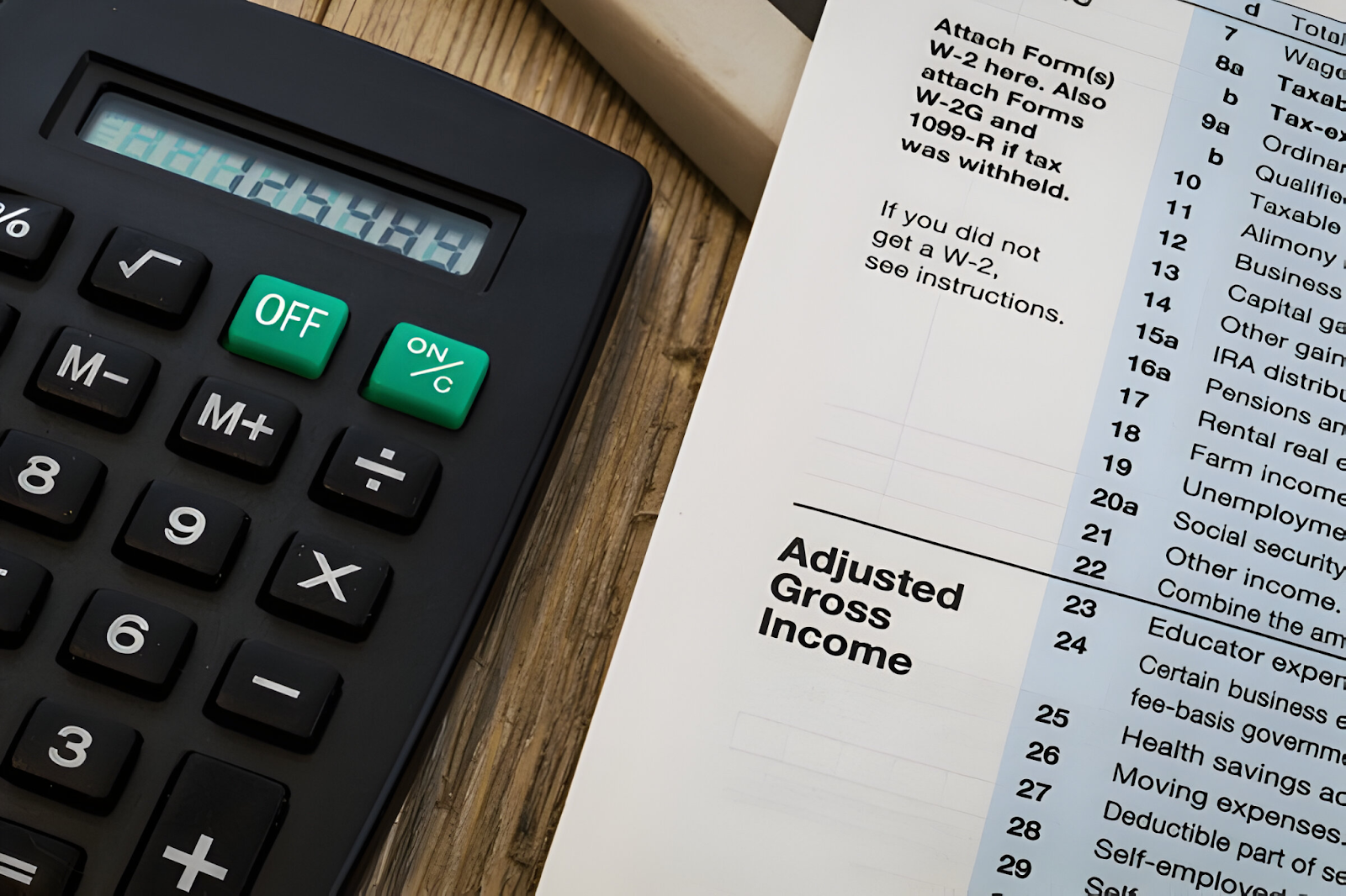 A close-up of a calculator and a tax form displaying "Adjusted Gross Income," representing the process of calculating gross pay in payroll processing.






