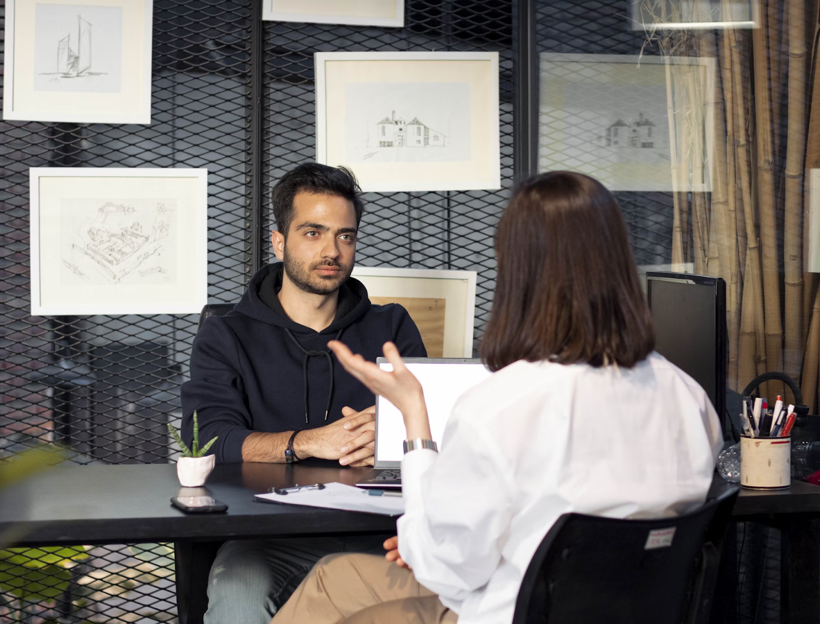 A female boss in a white dress interviews a young boy in a black hoodie, asking him to introduce himself