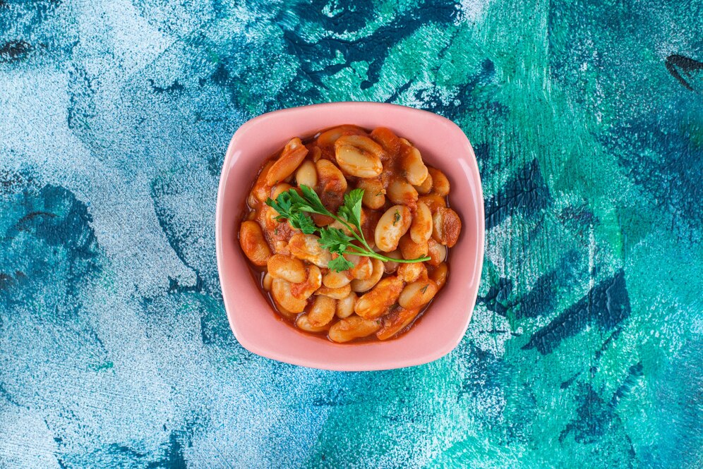 A pink color bowl full of baked beans