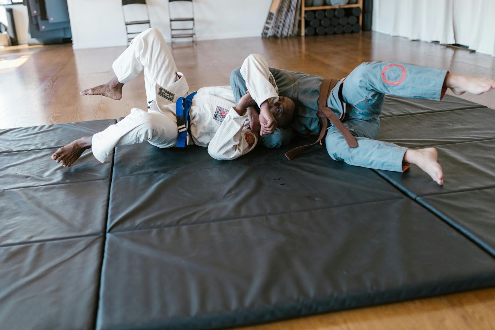 Two martial arts practitioners grapple on the ground during a training session.
