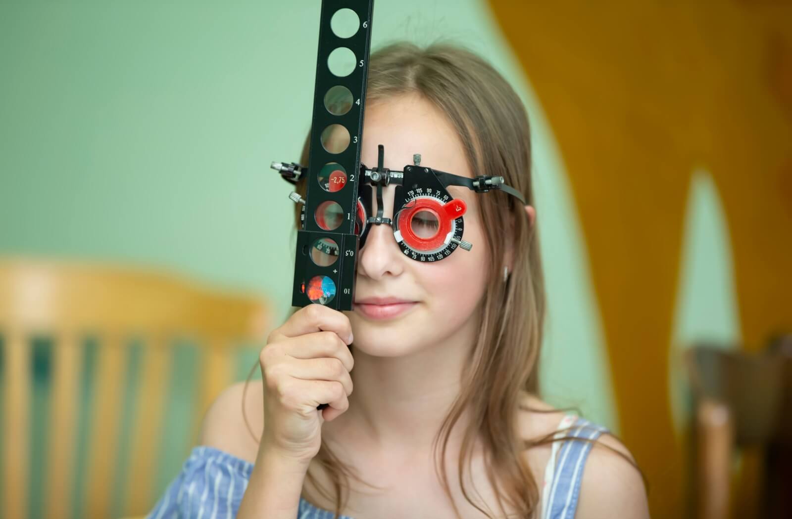 A teenager in vision therapy is shown wearing a special set of glasses with adjustable lenses while holding a stick with many lenses in front of their right eye.