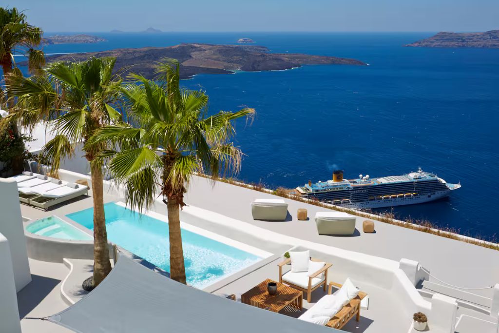 villa with palm trees blue pool and lounge chairs looking out onto a blue  ocean with a cruise ship