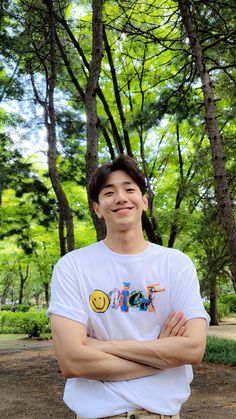 This contain an image of Nam Yoon Su standing in front of trees with his arms crossed and smiling 