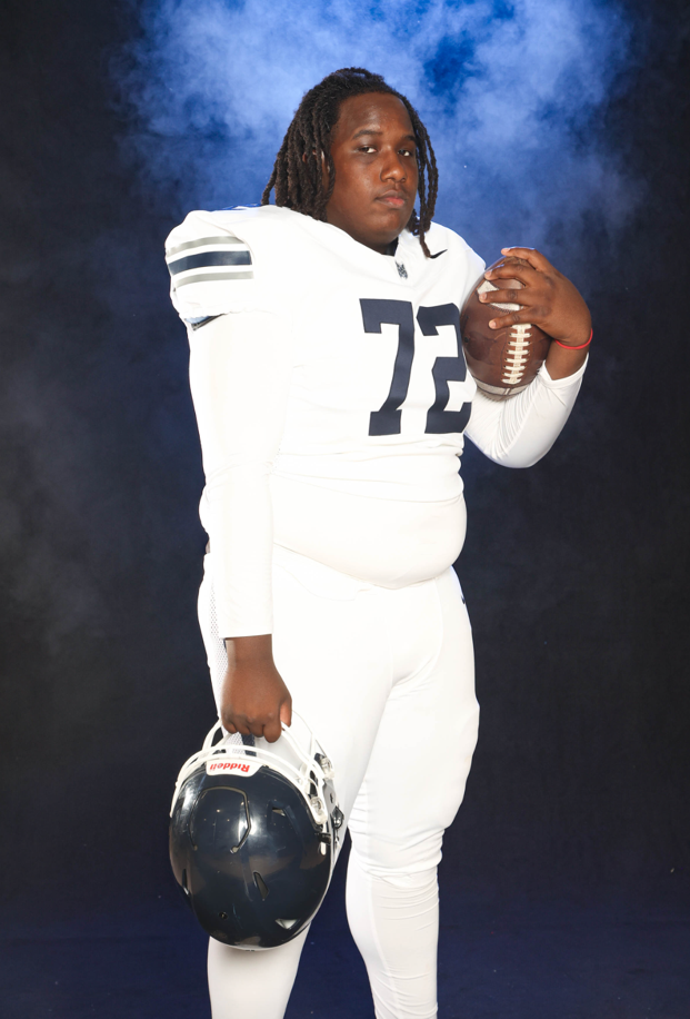 A person in a football uniform holding a football and a helmet

Description automatically generated