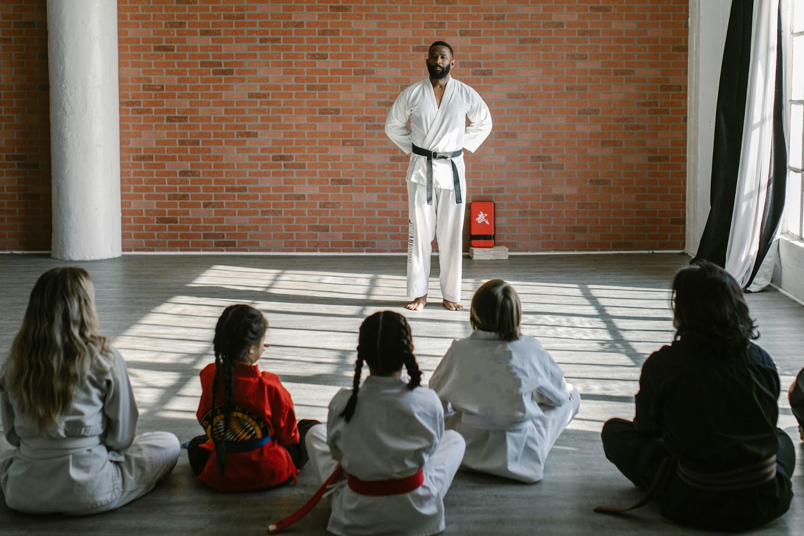 A martial arts instructor talking to a group of young students who are sitting on the floor