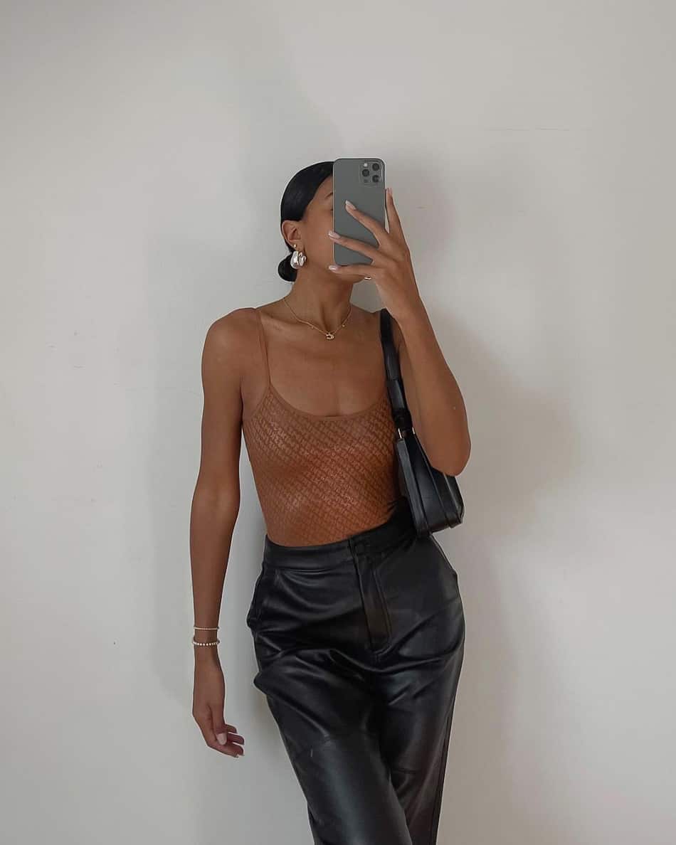 A woman wearing black leather pants and a brown skims bodysuit with a black handbag
