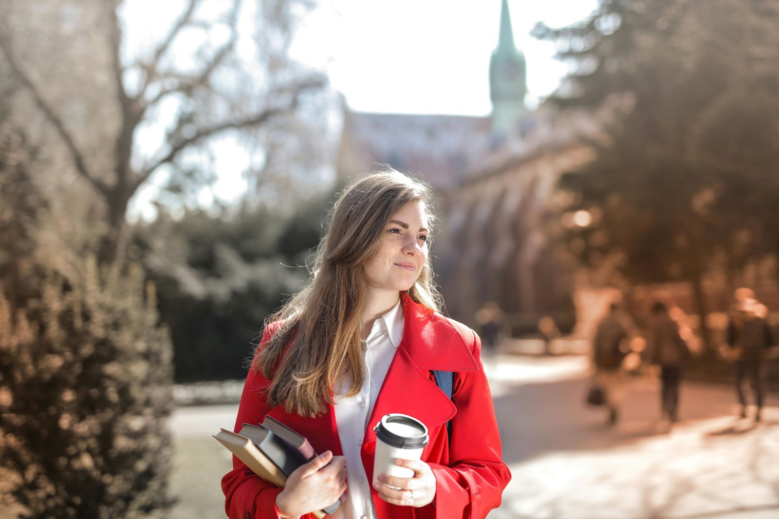 A female college student holding a coffe cup and some books