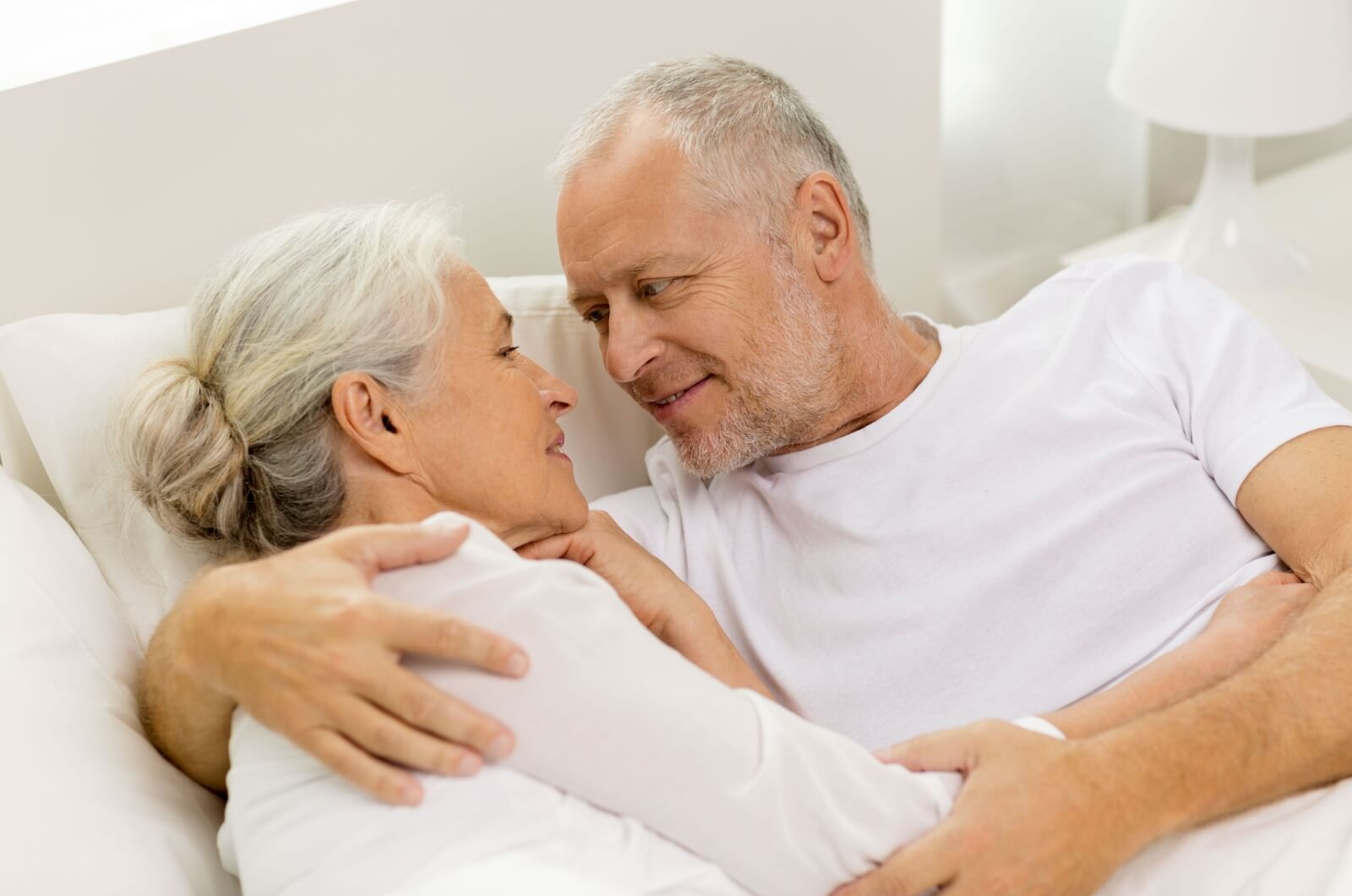 An older couple embracing each other in bed and having a conversation about sex.