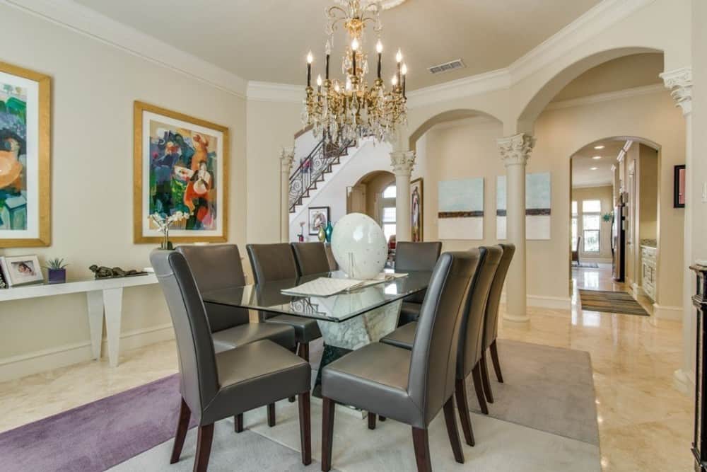 Formal dining room with leather upholstered chairs and a glass top dining table well-lit by a fancy chandelier.