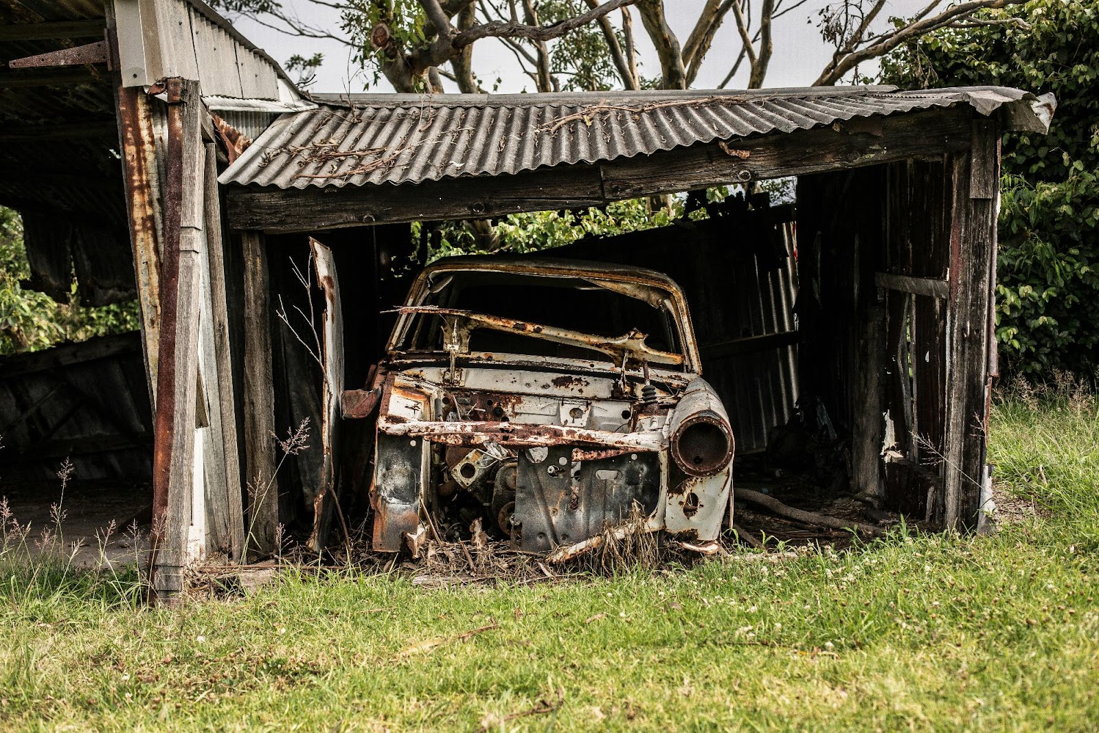 an old rusted out car in a shed