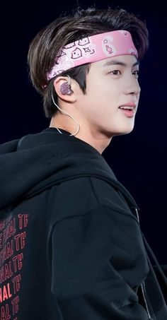 This contains an image of BTS Jin with ear buds wearing a pink headband