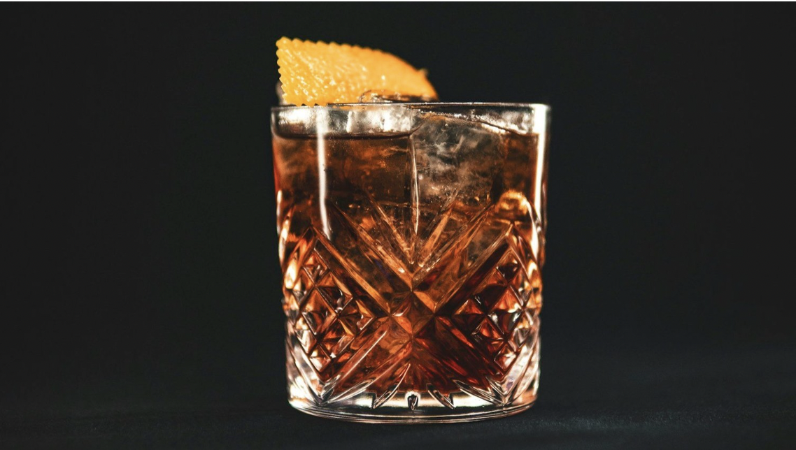 A negroni cocktail is in a crystal glass with ice and an orange peel garnish