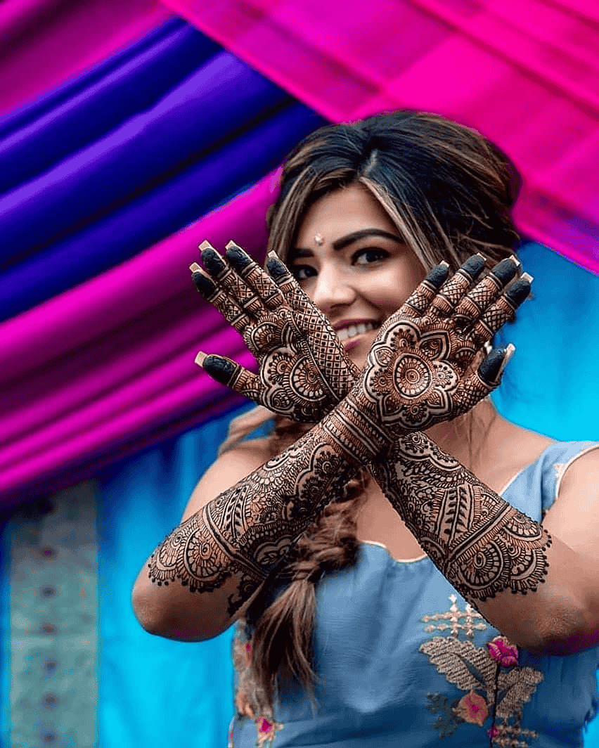 Mehndi photoshoot of a bride standing and showing her mehndi