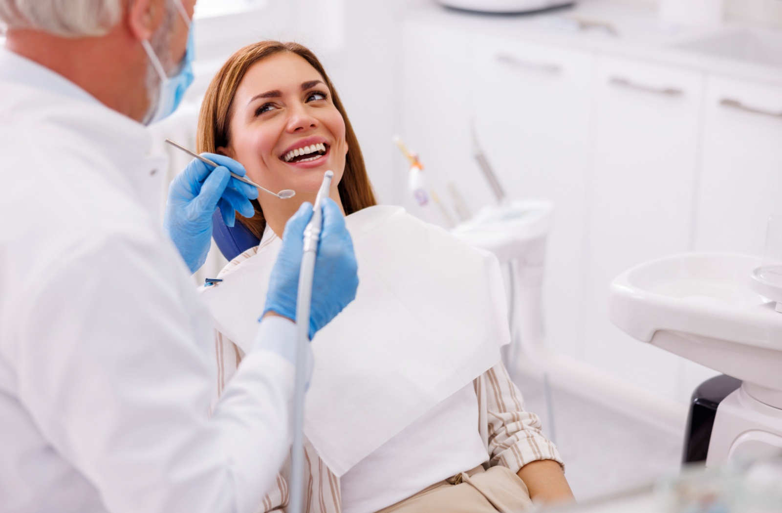 Female patient smiling during a dental check-up with a dentist examining her teeth.