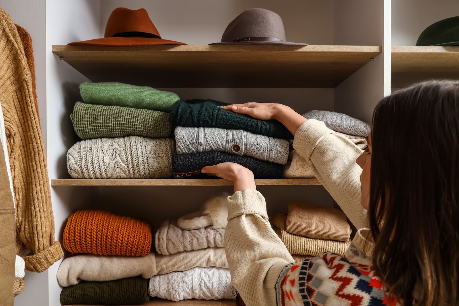 woman trying out different sweater storage ideas by folding and stacking fall colored sweaters