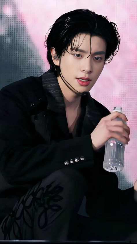 A picture of enhypen Jake on a black suit holding a bottle water 