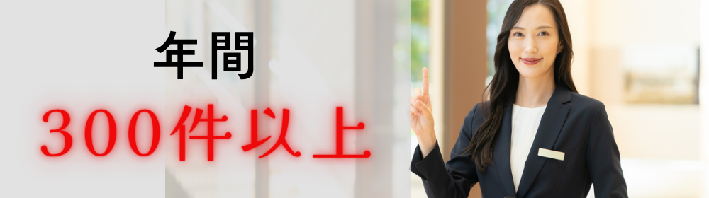 黒色文字で「年間」、赤色文字で「300件以上」と表記されたコピーを人差し指で示すスタッフの女性