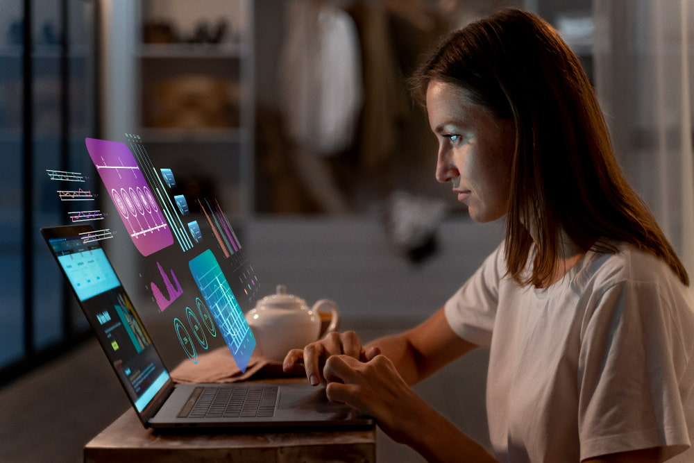 A woman using a laptop with projected digital charts on the screen.