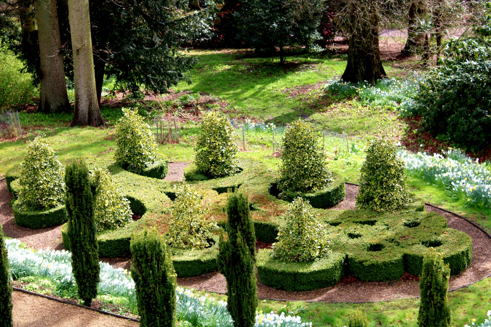 Photo of intricate landscaping featuring spiral-shaped trimmed bushes and a variety of plants and trees. 