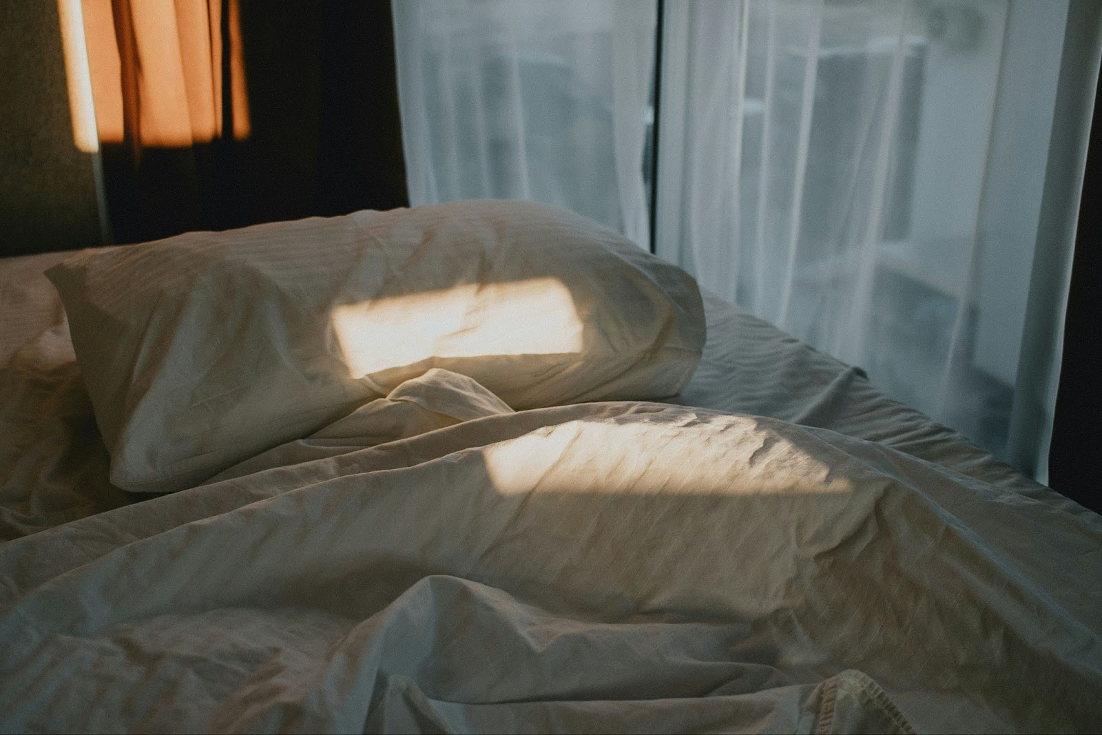 Bed slightly unmade with sunlight on the pillow