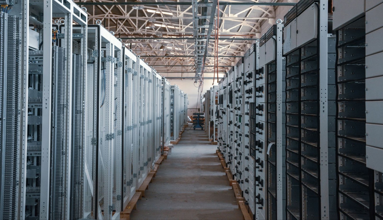 A long aisle of industrial server racks in a large, open facility with a high ceiling and visible wiring.
