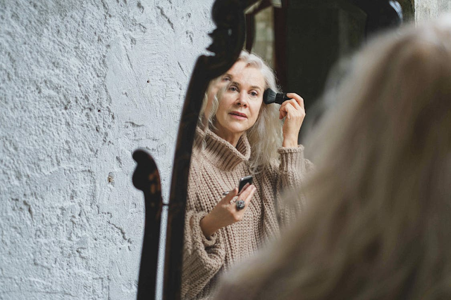older woman applying make up in mirror