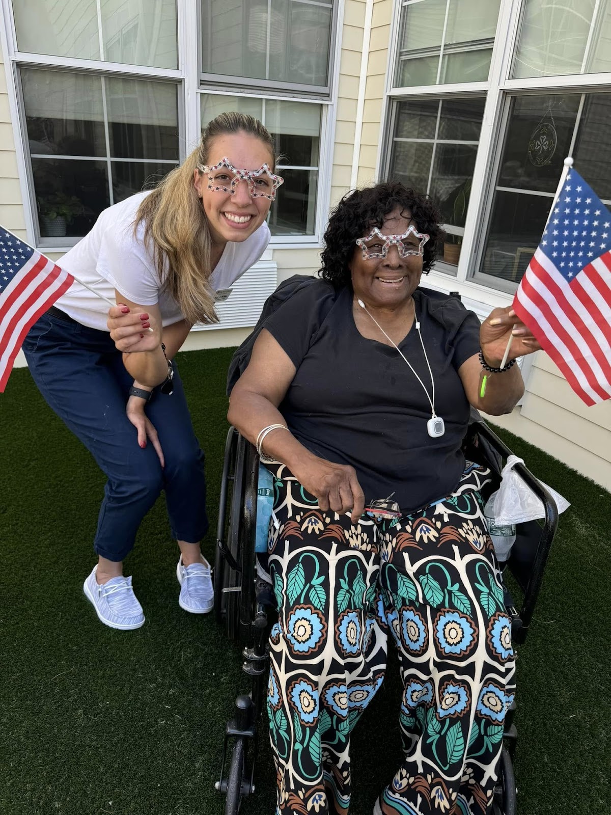 A picture of a senior care specialist smiling with a resident, both of whom are holding American flags